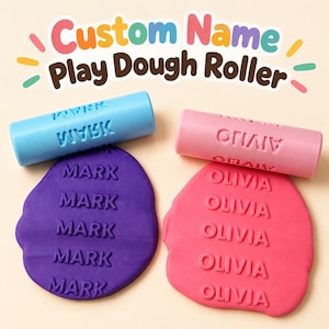 May include: Two cylindrical play dough rollers, one light blue and one pink, each featuring a custom name. The blue roller is embossed with the name MARK, and the pink roller is embossed with OLIVIA. The text Custom Name Play Dough Roller is visible.