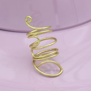 Può includere: Un anello a forma di spirale color oro. L'anello presenta una serie di fasce curve che si avvolgono attorno al dito, con un ricciolo decorativo in alto. L'anello è realizzato in un materiale metallico lucido ed è posto su uno sfondo rosa.