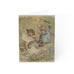 May include: Greeting card featuring a vintage illustration of three kittens in a garden setting. One kitten is wearing a blue dress and bonnet, reaching for a butterfly. The other two kittens are playing in the grass. The card is white.