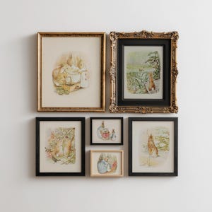 May include: A collection of framed art prints featuring illustrations of rabbits in various scenes. The frames vary in style, including ornate gold and simple black, creating a gallery wall aesthetic. The artwork has a vintage, storybook feel.