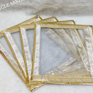 May include: A stack of gold saree covers with clear plastic windows. Each cover has a decorative gold border and a silver and gold patterned ribbon. The text "SINGLE SAREE COVER" is at the top.