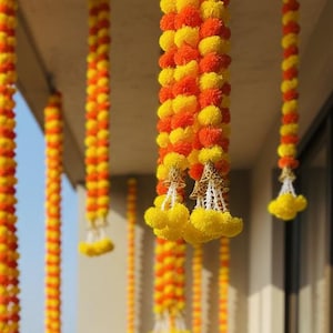 May include: A balcony decorated with strings of yellow and orange marigold flowers. The flowers are hanging from the ceiling and draped along the railing. A small table and chair set are visible on the balcony.