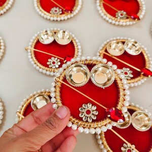 May include: Red and gold decorative plates with pearl and gem accents. Each plate features two small gold bowls and a decorative stick with a red gem. The plates are arranged on a white surface.
