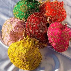 Könnte beinhalten: Sechs bestickte Kordelzugbeutel in Grün, Rot, Rosa, Gelb und Fuchsia. Jeder Beutel hat goldene Blumenstickereien und einen goldenen Kordelzugverschluss. Die Beutel sind auf einer weißen Satin-Oberfläche angeordnet.