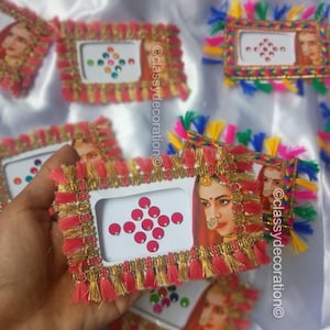 May include: Rectangular frames with a portrait of a woman, adorned with red and gold trim, and colorful tassels. The frames are decorated with small, colorful gems and are set against a white background.