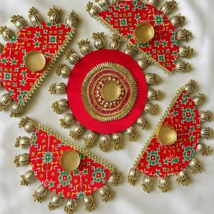 Op de afbeelding: Rode en gouden decoratieve items met een cirkelvormig middelpunt en waaiervormige stukken. Elk waaiervormig stuk heeft een goudkleurige beker en is versierd met goudkleurige kralen. De items hebben een rood patroon.
