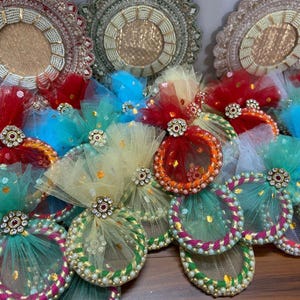 May include: A collection of colorful, decorative items. The items feature a circular design with intricate beadwork and are adorned with tulle and jewel accents. Colors include red, blue, green, and yellow.