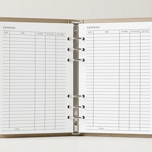 May include: Open beige binder with lined expense pages. The pages are labeled with "EXPENSES" at the top and include columns for date, item, income, outgoing, and balance. The binder is open, revealing the interior pages.