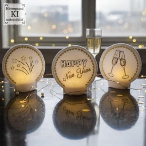 Puede incluir: Tres decoraciones redondas iluminadas con un tema festivo. Una presenta fuegos artificiales, otra dice "HAPPY New Year", y la tercera muestra copas de champ&aacute;n brindando. Cada una tiene un borde dorado y se encuentra sobre una superficie reflectante.