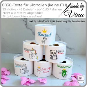 Op de afbeelding: Een stapel witte toiletpapierrollen, elk versierd met unieke borduursels. De rollen tonen verschillende afbeeldingen en teksten, waaronder een eenhoorn, een panda en de woorden "Thronsaal" en "Rollenkönig". Roze bloemblaadjes liggen op de bodem.