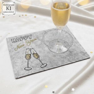 Puede incluir: Un mantel individual de fieltro gris con la inscripci&oacute;n bordada "HAPPY New Year" y dos copas de champ&aacute;n brindando. Una copa de champ&aacute;n con l&iacute;quido burbujeante est&aacute; sobre el mantel individual. El mantel individual est&aacute; sobre una superficie blanca con confeti de estrellas doradas.
