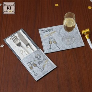 Puede incluir: Un juego de manteles individuales y portacubiertos de fieltro gris con texto dorado e ilustraciones de copas de champ&aacute;n. El mantel individual tiene una copa de champ&aacute;n con una bebida. El portacubiertos contiene un tenedor y un cuchillo. El texto dice "Happy New Year".