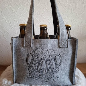 Graue Filztasche für Bierflaschen, bestickt mit zwei anstoßenden Bierkrügen und Hopfenranken.

Grey felt beer carrier bag embroidered with two clinking beer mugs and hop vines.