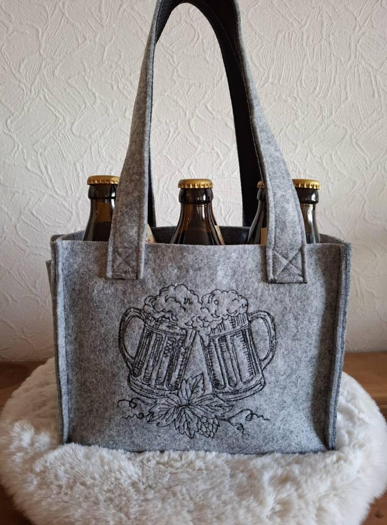 Graue Filztasche für Bierflaschen, bestickt mit zwei anstoßenden Bierkrügen und Hopfenranken.

Grey felt beer carrier bag embroidered with two clinking beer mugs and hop vines.