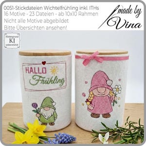 May include: Two white cylindrical containers with wooden lids. One features a green gnome with a purple flower, the other a pink gnome with a daisy. Text on one reads "HALLO Frühling". A pink ribbon adorns the second container.
