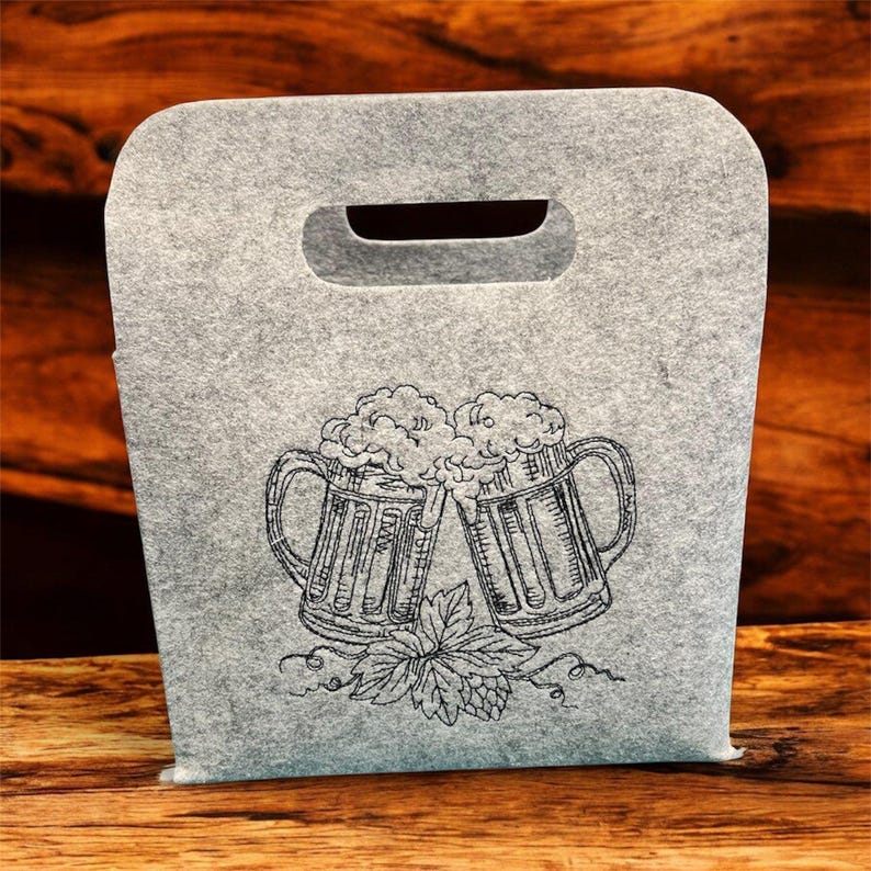 Graue Filztasche mit zwei gestickten, schäumenden Bierkrügen und Hopfenblättern im Scribble-Stil.

Grey felt bag with two embroidered, foaming beer mugs and hop leaves in scribble style.