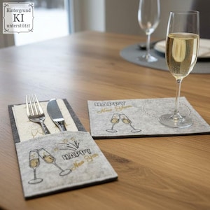 Puede incluir: Una mesa festiva con una copa de champ&aacute;n llena de una bebida burbujeante. Se ven dos manteles individuales de fieltro gris con texto dorado e ilustraciones de copas de champ&aacute;n. Un mantel individual contiene un tenedor, un cuchillo y una servilleta. El texto en los manteles es "HAPPY New Year."