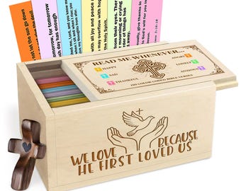 Könnte beinhalten: Eine Holzkiste mit Scharnierdeckel, die farbige Karten mit Bibelversen enthält. Die Kiste ist mit einem Kreuz, einer Taube und Händen verziert. Der Text auf der Kiste lautet "WE LOVE BECAUSE HE FIRST LOVED US."