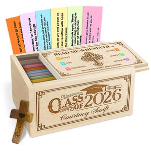 Op de afbeelding: Een houten kist met de tekst "Class of 2026 Courtney Swift" en een afstudeerhoedontwerp. De kist bevat kleurrijke kaarten met bijbelverzen. Een houten kruis met een hart staat aan de zijkant.