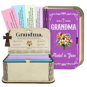 May include: A wooden box set with a Bible-shaped cover and a card holder. The cover is purple with the word "Grandma" and a floral design. The card holder has colourful cards with inspirational quotes. A wooden cross charm is attached.