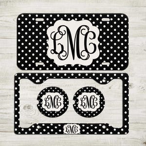 May include: Black and white polka dot car accessories set. Includes a license plate, license plate frame, two car coasters, and a small emblem. Each item features a white monogram on a black background.