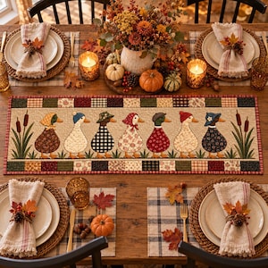 Pode incluir: Um caminho de mesa retangular de tecido com um design acolchoado que apresenta sete patos com vários chapéus e roupas, posicionados entre taboas. A borda consiste em um padrão de patchwork em tons de vermelho, verde, marrom e creme.
