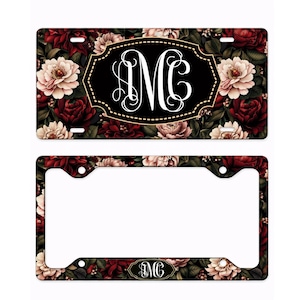 May include: A license plate and frame featuring a floral design with burgundy and cream-colored flowers on a dark background. The license plate has a black oval with the white letters "MC". The frame has a matching floral pattern.