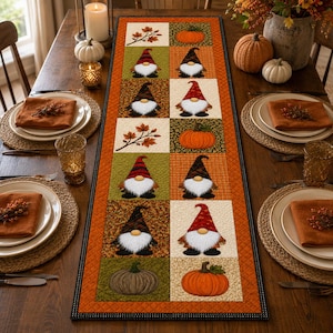 Può includere: Un runner da tavola rettangolare in tessuto con un design patchwork di quadrati a tema autunnale. Il motivo include illustrazioni di gnomi con cappelli alti, zucche arancioni e foglie autunnali marroni su sfondi verdi, arancioni e crema.