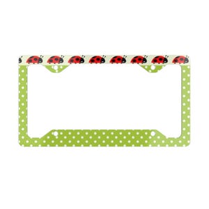 May include: A license plate frame with a light green background and white polka dots. The top of the frame features a row of red ladybugs with black spots. The frame is designed to fit a standard license plate.