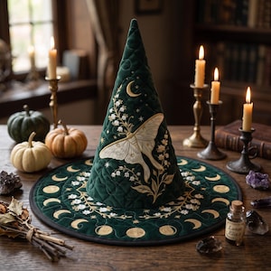 May include: A dark green quilted cone-shaped hat featuring gold embroidered moon phases along the brim, a large central moth illustration, and delicate lily of the valley floral patterns. The hat has a structured, pointed silhouette.