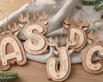 May include: Wooden Christmas ornaments shaped like reindeer with letters and names. The ornaments are in the shape of the letters A, S, D, J, and C. Each ornament has a natural wood finish with a lighter wood inlay.