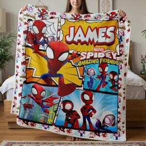 May include: A colorful Spidey and His Amazing Friends blanket featuring a comic book style design. The blanket has a white border with Spider-Man graphics and the name "JAMES" in large letters. The Marvel logo is also visible.
