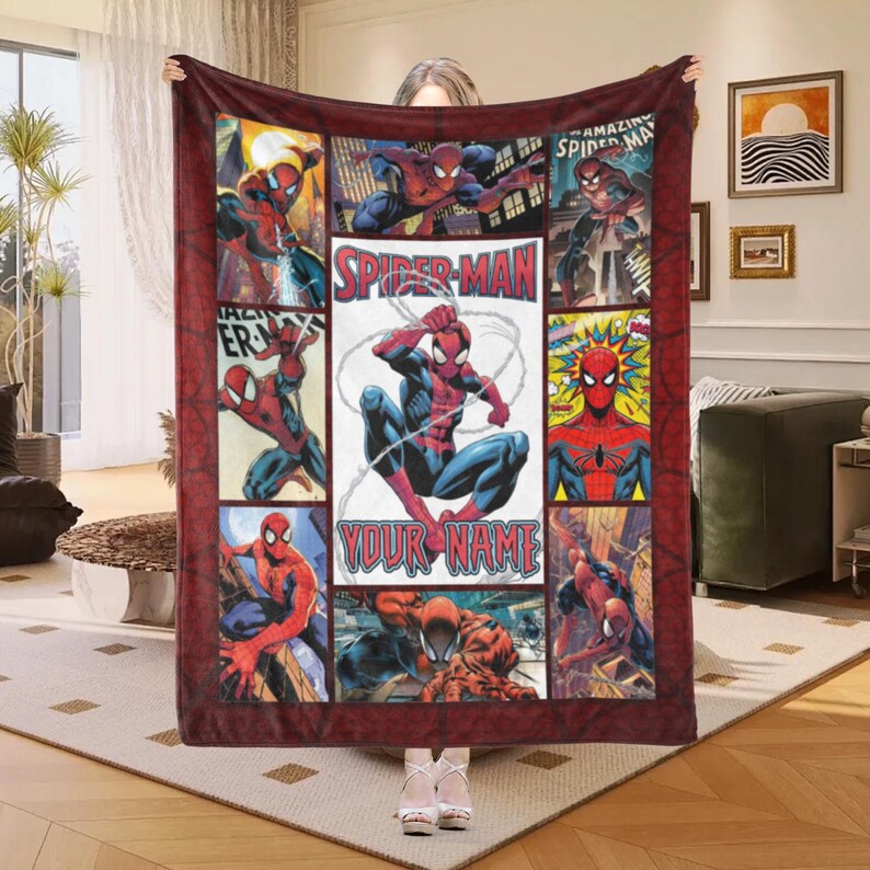 Op de afbeelding: Een rechthoekige, rood-zwarte Spider-Man deken met stripboekpanelen. Het middenpaneel heeft de tekst "Spider-Man" en "Your Name". De deken wordt door een persoon omhoog gehouden.