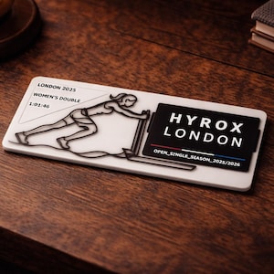 May include: A white rectangular plaque with a black outline of a person running, and the text "HYROX LONDON" in black. The plaque also includes the text "LONDON 2025 WOMEN'S DOUBLE 1:01:46".