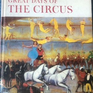 May include: A vintage book cover with a colorful illustration of a circus scene. The cover features the title "Great Days of The Circus" and the logo "American Heritage Junior Library".