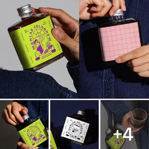 Pode incluir: Garrafas quadradas de vidro de café cold brew com tampas prateadas. As garrafas têm rótulos coloridos com o texto "MANLAB COLDBREW" e ilustrações. Um rótulo é rosa com um padrão de grade. O café parece marrom escuro.