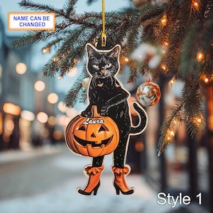 May include: A black cat-shaped Halloween ornament holding a carved pumpkin. The cat wears orange boots and has the name "Laura" on the pumpkin. The ornament hangs from a gold string, with the text "NAME CAN BE CHANGED" at the top.