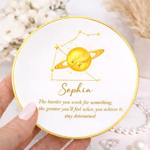 May include: White ceramic plate with a gold rim, featuring a golden planet design and the name "Sophia." The plate includes the text: "The harder you work for something, the greater you'll feel when you achieve it, stay determined."