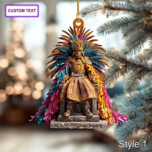 May include: Ornament featuring a detailed figure of a person in ornate Aztec-inspired attire, including a feathered headdress and colorful cape. The figure is seated on a stone throne. The ornament has the text "Custom Text" and "Style 1".