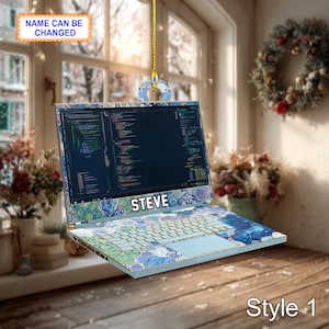 Puede incluir: Adorno navideño con forma de portátil con un diseño floral azul y blanco. La pantalla muestra código y el nombre "STEVE" está impreso en el teclado. El texto "NAME CAN BE CHANGED" está en la parte superior y "Style 1" en la inferior.