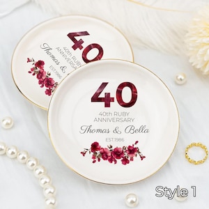 May include: Two white ceramic plates with gold rims, featuring a ruby red "40" and floral design. Text reads "40th Ruby Anniversary" and "Thomas & Bella EST.1986". One plate has "Thomas &" and the other has "Thomas & Bella".