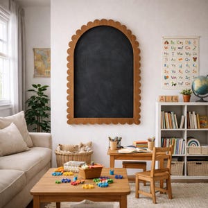 Puede incluir: Una pizarra con marco de madera y borde festoneado cuelga de una pared blanca. Una habitación infantil está amueblada con una mesa de madera, una silla y una estantería blanca. También se ve una colorida tabla del alfabeto y un globo terráqueo.