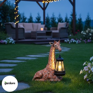 以下が含まれることがあります： ブロンズ色のキリンの像が、電球の灯った黒いランタンを持っています。キリンは緑の芝生の上に横たわっており、背景にはパティオとストリングライトがあります。この像は、庭の装飾品です。