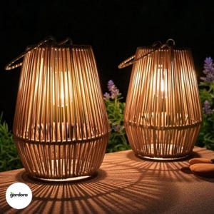 May include: Two illuminated, cylindrical lanterns with a woven bamboo design. Each lantern has a metal handle and casts a warm glow. The lanterns are placed on a wooden surface, with shadows from the bamboo visible.