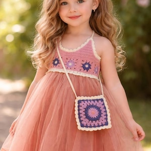 May include: A little girl wearing a pink crochet top and a matching tulle dress. The top has a floral design, and she carries a small square purse with a similar crochet pattern. A flower hair clip adorns her hair.