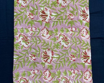 May include: Pink fabric with a floral pattern. The design features large white flowers with red and green accents, surrounded by green leaves and vines. The fabric is suspended from a wooden clothes hanger.