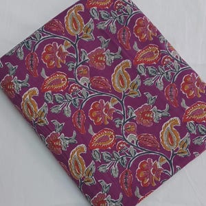 May include: Folded fabric with a vibrant floral pattern. The design features paisley shapes and flowers in shades of orange, red, and yellow against a deep purple background. Gray vines and leaves complete the design.