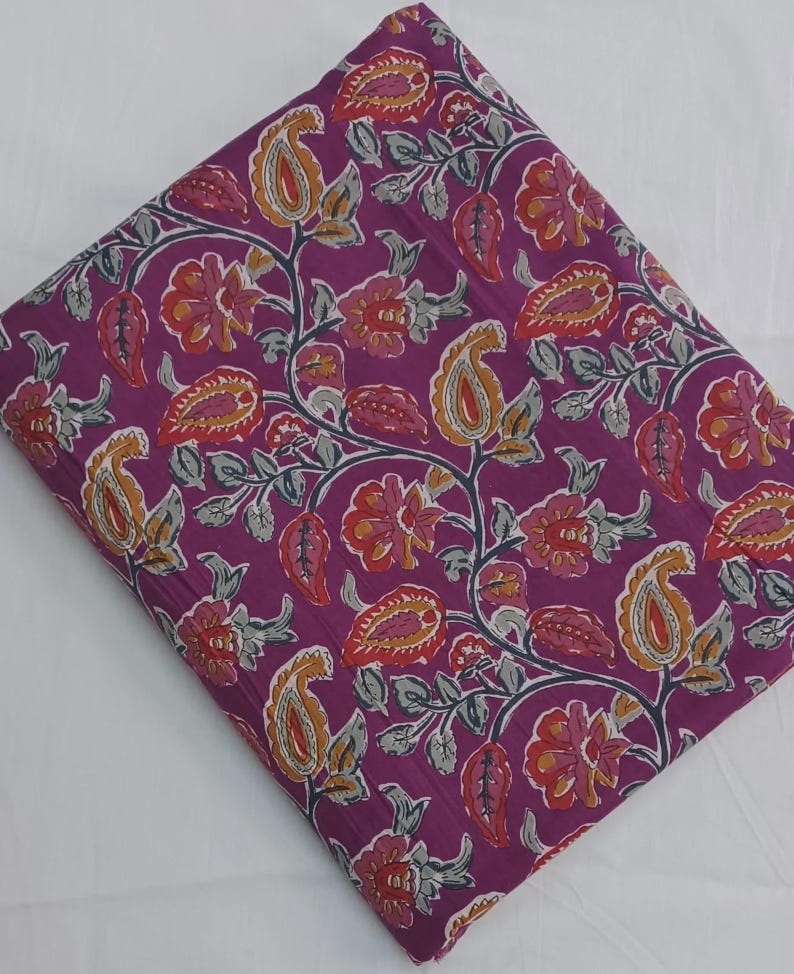 May include: Folded fabric with a vibrant floral pattern. The design features paisley shapes and flowers in shades of orange, red, and yellow against a deep purple background. Gray vines and leaves complete the design.