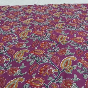 May include: A large piece of fabric with a repeating floral pattern. The design features paisley and floral elements in shades of red, orange, yellow, and gray against a deep purple background. The fabric appears to be cotton or a similar material.