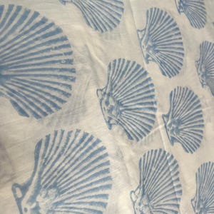 May include: A white fabric featuring a repeating pattern of light blue seashell prints. The shells are arranged in a staggered layout across the surface, displaying detailed ridges and a fan-like shape characteristic of scallop shells.